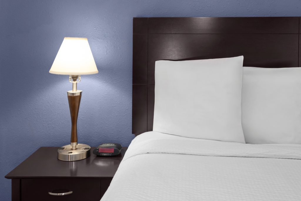 Bedside table with lamp, alarm clock and charging outlets at Travelodge by Wyndham Milwaukee